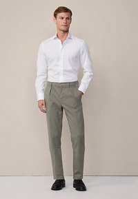 Witte overhemd met knopen gecombineerd met lichtgrijze broek met rechte pasvorm. Model draagt zwarte schoenen, minimalistisch ontwerp, neutrale achtergrond.