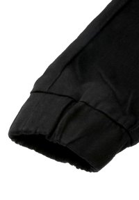 Schwarze Baumwollhose mit einem gerafften Saum. Der Stoff ist glatt mit einem leichten Glanz, hat ein einfaches, klares Design und keine Verzierungen.