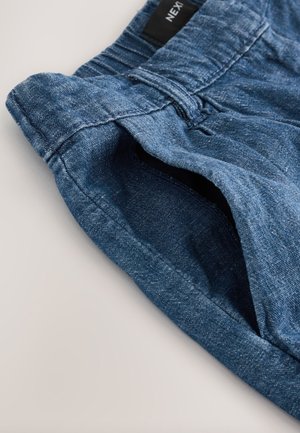 Siniset farkkushortsit, joissa on teksturoitu pinta. Vyötäröllä lenkit ja sivutaskut, jotka korostavat rentoa tyyliä.