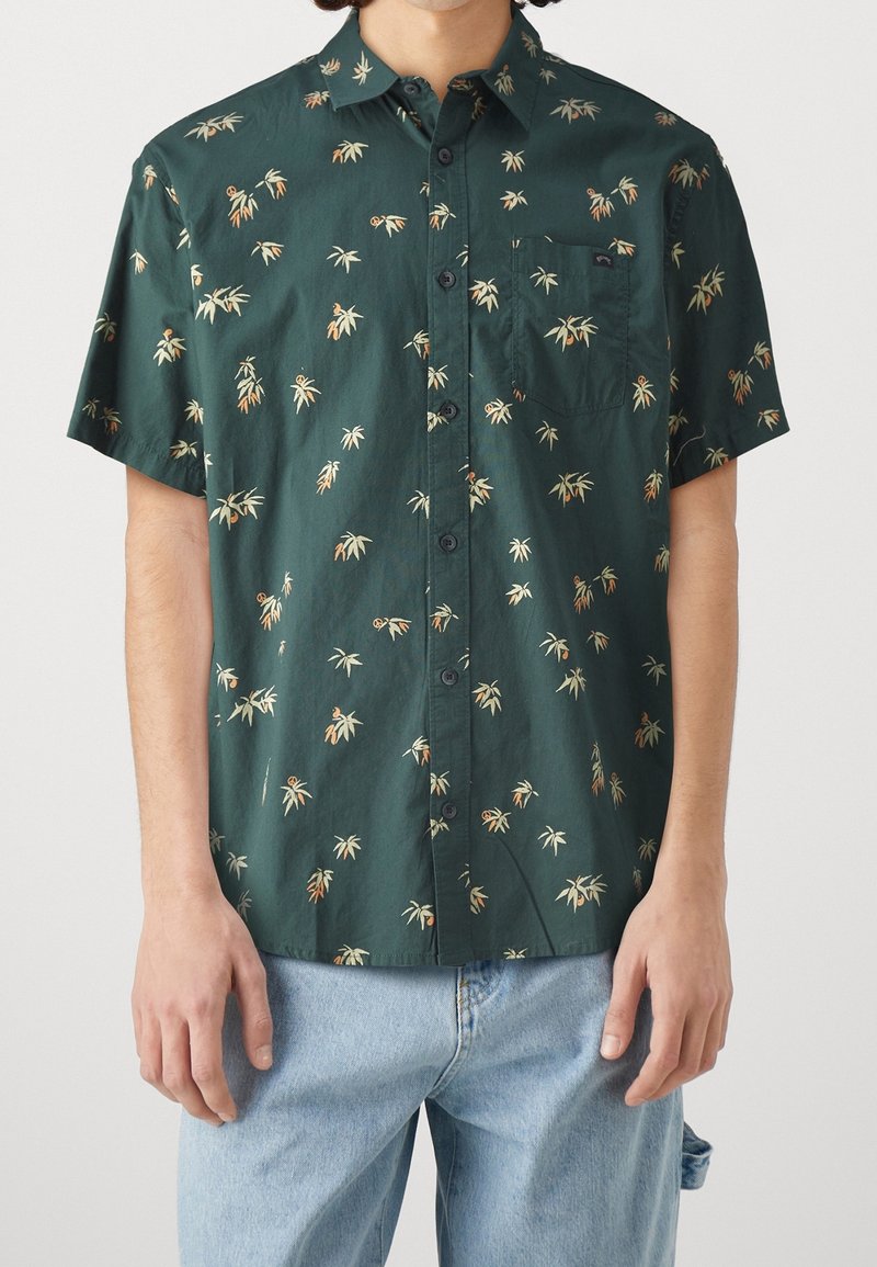 Chemise à manches courtes en coton vert foncé avec un motif de feuilles de palmier. Dotée d'un col boutonné et d'une poche poitrine avec un petit logo.