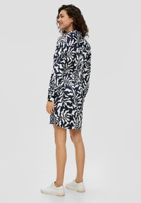 Langärmliges Kleid in marineblauem und weißem abstrakten Muster, mit einer taillierten Taille und einem ausgestellten Rock, kombiniert mit weißen Turnschuhen.