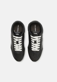 Black sneakers with a smooth leather upper, white laces, rounded toe, and branded heel. Includes decorative stitching and a logo on the side.