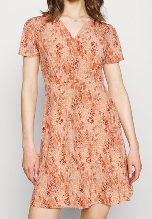 Mujer vistiendo un vestido floral de color melocotón con mangas cortas y escote en V, decorado con patrones de flores rojas y naranjas.