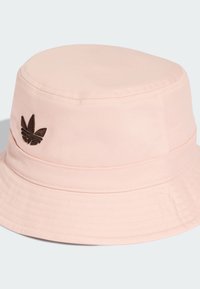 Světle růžový kšiltovka vyrobená z texturované tkaniny. Na přední straně má hnědé vyšívané logo a široký, strukturovaný okraj.