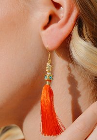 Goldfarbene Creolen mit einer dekorativen Perle mit türkisen Akzenten und einem lebhaften orangefarbenen Quasten, die eine feine Textur und ein detailliertes Design präsentieren.