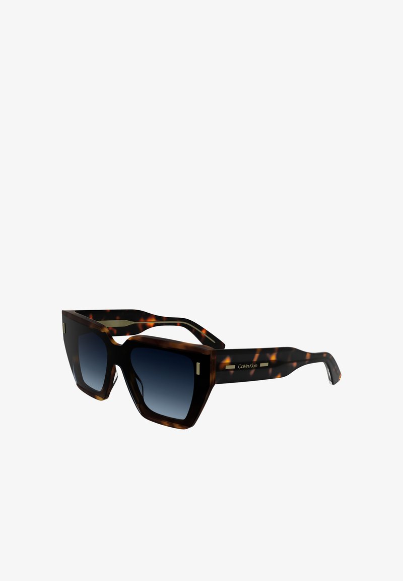 Okuliare z korytnačej škrupiny s uhlovými rámami, tmavými gradientnými šošovkami a zlatými akcentmi. Na ramenách sa nachádza výrazné logo Calvin Klein.