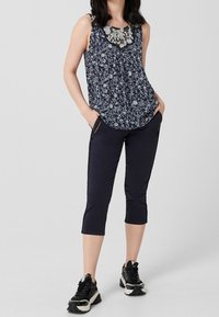 Granatowy kwiatowy top bez rękawów z koronkowym dekoltem, w zestawie z granatowymi spodniami capri i czarnymi trampkami z białymi akcentami. Prosty i funkcjonalny strój.