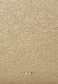 Beige tekstureeritud kunstnahast pind väikese kuldse "ANNA FIELD" logoga allservas. Sile viimistlus koos peenikese struktuuriga.