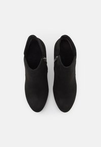 Paire de bottines noires en daim avec fermetures éclair latérales, vues de dessus sur fond blanc.