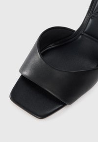 Čierne kožené sandále na slide s širokým horným pásom a štvorcovým dizajnom špičky. Hladká textura s plochou podrážkou. Minimalistická estetika.