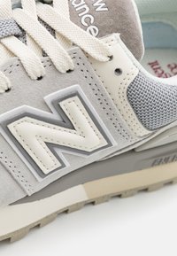 Baskets gris clair avec une tige en suède et mesh, accents beige, grand logo blanc "N" et semelle en caoutchouc texturée.