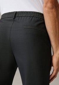 Black pants with a smooth, textured finish, featuring a gathered waistband, side pockets, and a tailored, slim fit design.