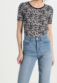 Top de manga corta en azul marino y crema con un patrón y cuello redondo, combinado con unos pantalones de mezclilla claros de tiro alto que tienen un cierre con botón.
