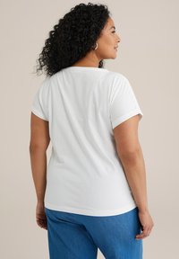 Camiseta blanca de manga corta hecha de una tela suave, con puños enrollados y un corte relajado, combinada con pantalones de mezclilla azul.