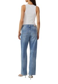 Lichtblauwe high-waisted jeans met een relaxte pasvorm, voorzien van achterzakken en een rafelige zoom. gecombineerd met een witte tanktop en zilveren sandalen.