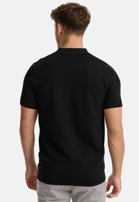 Black short-sleeve polo shirt featuring a textured knit fabric, a collared neckline, and ribbed cuffs. Fitted silhouette with a straight hem.