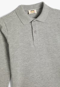 Grå polo t-shirt gjord av bomullsblandat tyg. Har en ribbad krage, treknapplång och en mjuk, texturerad yta.