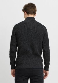 Dunkelgrauer gerippter Pullover mit hohem Kragen und langen Ärmeln, der ein strukturiertes Strickmuster und enganliegende Bündchen aufweist; getragen mit schwarzen Hosen.