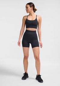Schwarzes Sportoutfit bestehend aus einem schicken Crop-Top mit dünnen Trägern und hochgeschnittenen Shorts. Hergestellt aus elastischem, strukturiertem Stoff.