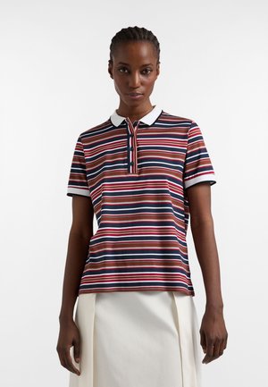 Donna che indossa una polo a maniche corte a righe multicolori con colletto bianco e una gonna color crema su uno sfondo neutro.