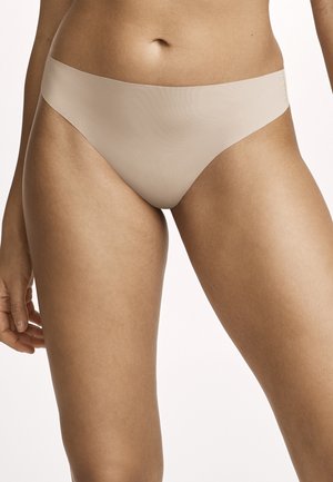 Female torso and upper legs wearing seamless beige bikini-style underwear against a neutral background.