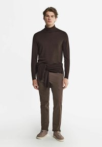 Mörkbrun stickad polotröja som matchas med bruna byxor. Tröjan har en knuten del vid midjan. Grå sneakers fulländar outfiten.