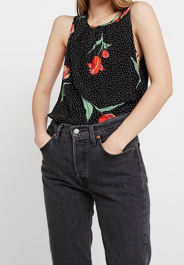 Haut noir sans manches à pois blancs et motif floral de tulipes rouges ; associé à un jean denim foncé avec boutons argentés et poches.