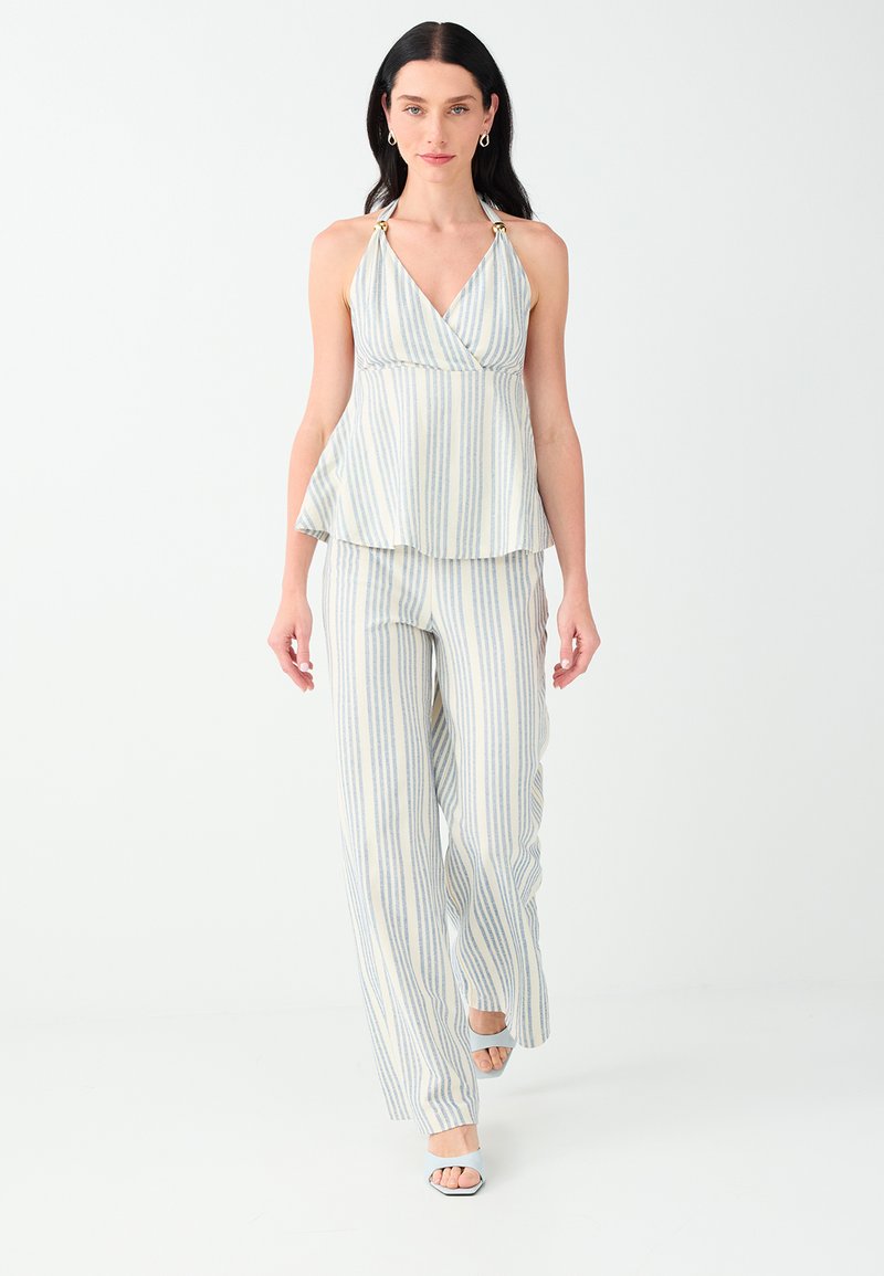 Femme aux longs cheveux foncés portant un débardeur rayé bleu clair et blanc et un pantalon large assorti, marchant en avant avec des talons blancs.
