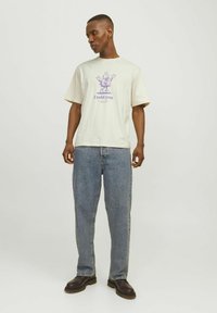 Light beige cotton T-shirt with purple graphic text "I told you" and cartoon design. Paired with relaxed blue jeans and black boots.