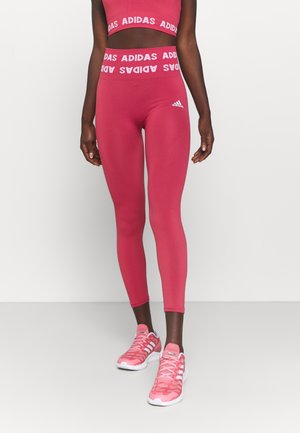 Leggings de sport roses ajustés avec une large ceinture portant le logo blanc "ADIDAS". Texture lisse et accents en relief sur les jambes.