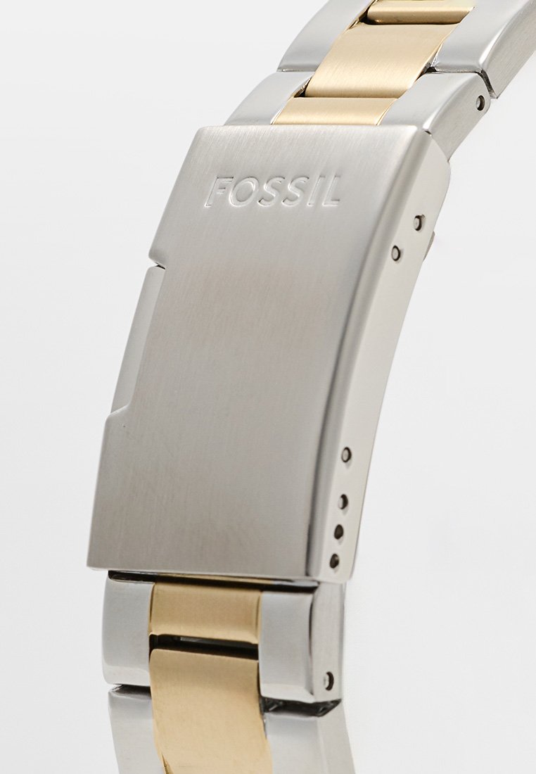 Bracciale in metallo tono argento e oro con una finitura liscia e lucida, caratterizzato dal logo "FOSSIL" e da maglie regolabili per la personalizzazione della misura.