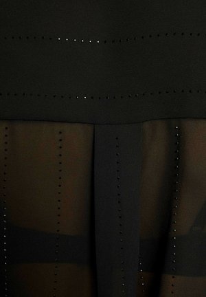 Abito nero con design a strati, con una parte superiore opaca e un pannello inferiore trasparente. Distintivi chiodini neri disposti in file orizzontali.