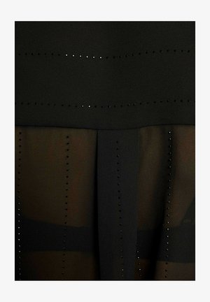 Abito nero con design a strati, con una parte superiore opaca e un pannello inferiore trasparente. Distintivi chiodini neri disposti in file orizzontali.