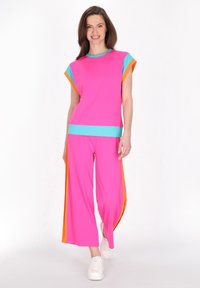 Lys pink to-delt outfit lavet af blødt stof, der har en kortærmet top med turkise detaljer og brede bukser med orange striber.