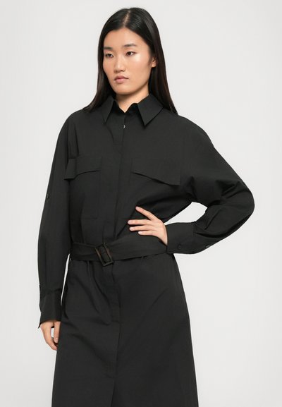 Black button-up shirt dress with two chest pockets, long sleeves, and a belted waist. Features a relaxed fit and smooth fabric texture.