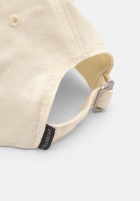 Tan cotton baseball cap with adjustable strap. Features a stitched seam and a small black label reading "PULL&BEAR." Soft texture.