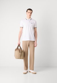 Hvit polo skjorte med svart kant, beige bukser og en brun lærveske. Vesken har glidelås og doble hanke. Uformelle hvite joggesko.