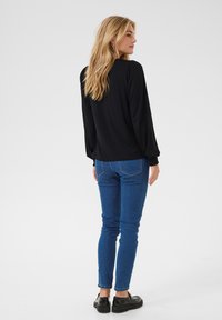 Black long-sleeve blouse with subtle puffed shoulders, paired with blue skinny jeans and black platform shoes, viewed from the back.