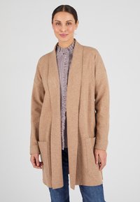 Cardigan lungo color marrone chiaro realizzato in tessuto morbido. Presenta un'apertura frontale, due tasche frontali e polsini a coste. Indossato sopra una blusa a righe.