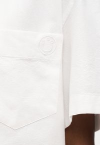 Manche et poche d'un vêtement blanc avec un logo smiley en relief subtil dans le coin de la poche.