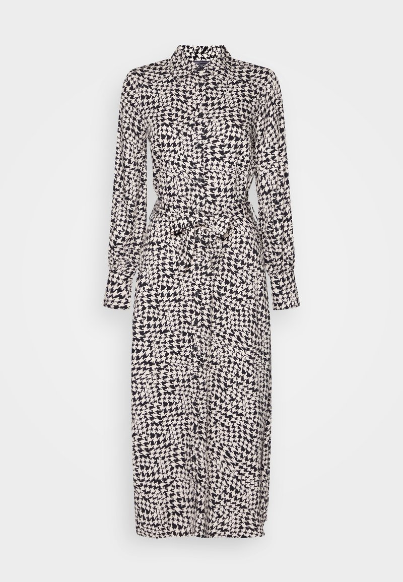 Vestido largo con botones, que presenta un patrón de pata de gallo en negro y crema. Tiene una cintura anudada y mangas largas, confeccionado en un tejido ligero.