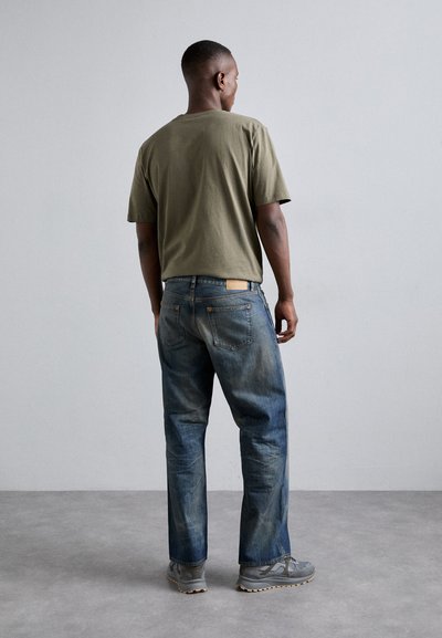 T-shirt vert olive, coupe décontractée. Jean bleu usé avec un léger délavage et deux poches arrière. Baskets grises avec semelle texturée.