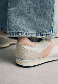 Sneakers i hvid og pink farveskema; ruskind- og lædermaterialer; teksturerede detaljer; lavprofil design; gummisål; slidte denimjeans.