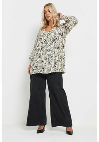 Blommig blus med krämfärgad bakgrund, prydd med svarta linjeteckningar av blommor, en V-ringning och långa ärmar, kombinerad med vida svarta byxor.
