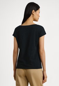 Juoda medvilninė trumpomis rankovėmis marškinėliai su plačiu kaklu, laisvo stiliaus ir lygiu paviršiumi. Pasižymi minimalistiniu dizainu be matomų raštų.