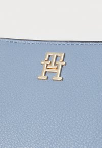 Light blue textured leather surface featuring a metallic gold logo emblem with interlocking letters design.