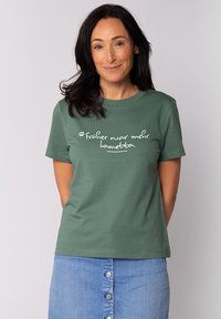 Grünes Baumwoll-T-Shirt mit kurzen Ärmeln, das auf der Vorderseite weißem Text mit der Aufschrift "früher war mehr lametta" zeigt. Schlichtes, lässiges Design.