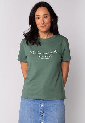 Grünes Baumwoll-T-Shirt mit kurzen Ärmeln, das auf der Vorderseite weißem Text mit der Aufschrift "früher war mehr lametta" zeigt. Schlichtes, lässiges Design.