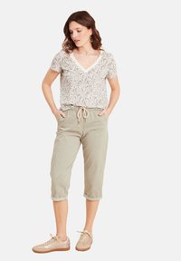 Lichtgrijs gestreept T-shirt met V-hals, gecombineerd met beige cropped broeken met verstelbare trekkoorden en opgerolde boorden, en beige sneakers.