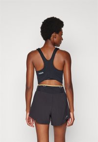 Svart atletisk tanktop med racerback-design och logodetalj, kombinerad med svarta shorts med gul midja och sidodetaljer.